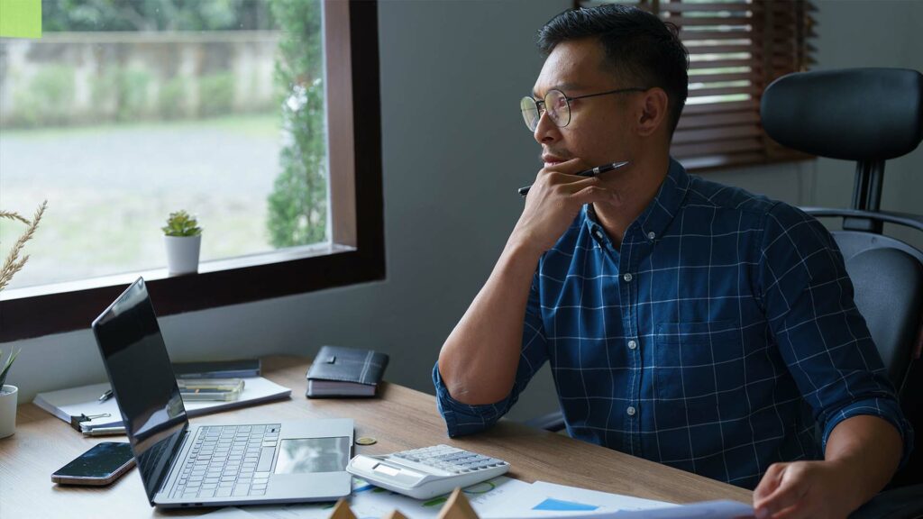 Businessman sitting at a computer looking pensively into the distance