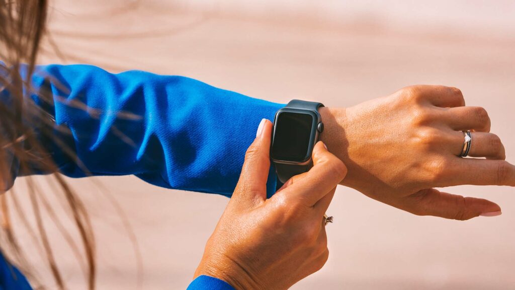 Woman looking at and touching smartwatch on her arm.