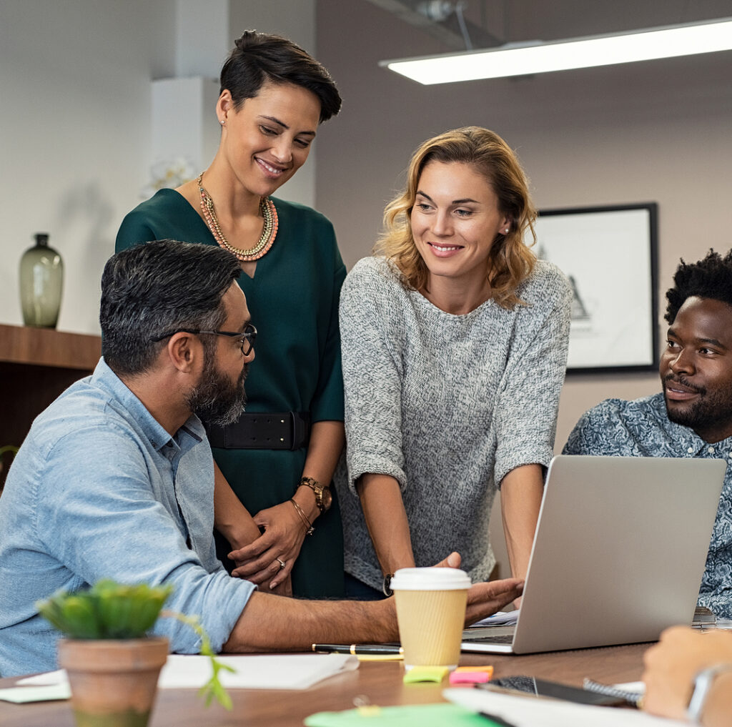 Multiethnic business people talking and smiling during meeting in office. Mature middle eastern man explaining proposal. Happy businessman showing project and marketing strategy on laptop to colleague