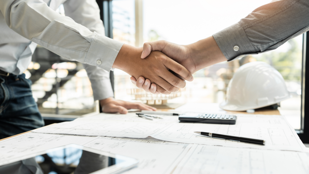 Professionals shaking hands over a drafting table