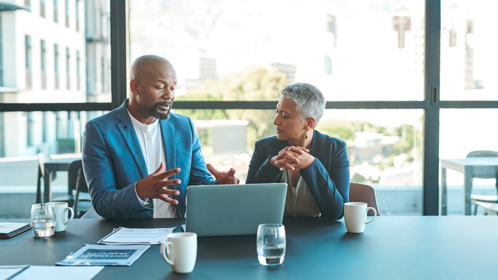 Two professionals in a board room talking in front of a computer