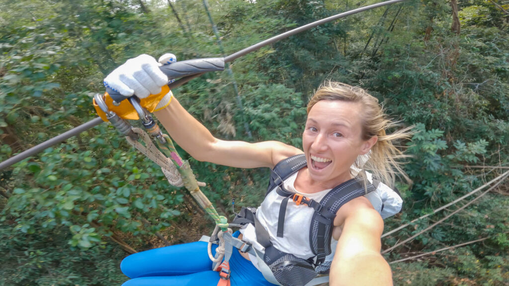 Woman ziplining through trees holding and look at the camera