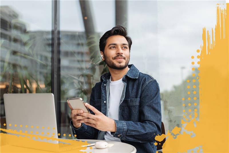 Man sitting outside working on laptop, listening to music on his phone