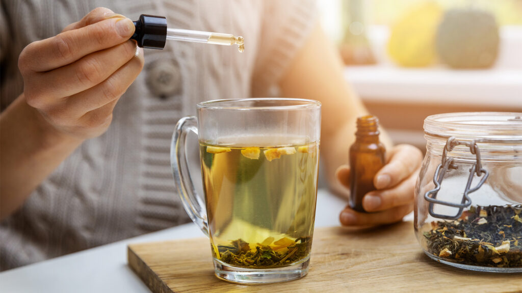 Closeup picture of man using a dropper, adding tincture to mug of tea