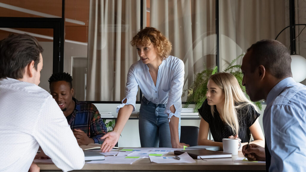 Businesswoman leaning over table and discussing strategy with a team.
